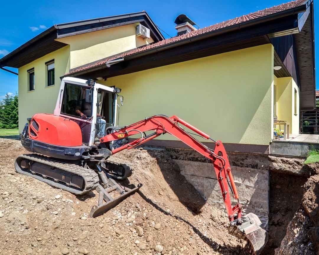 Excavator digging near house foundation