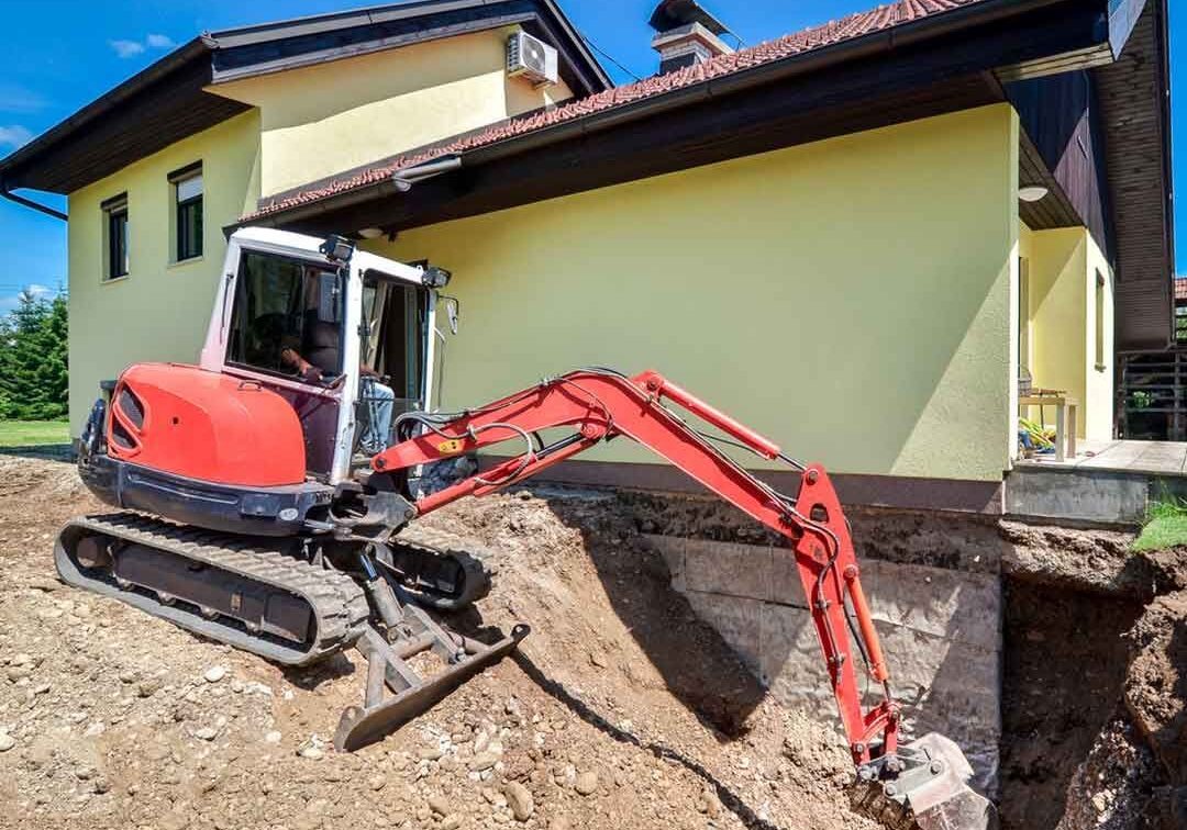 Excavator digging near house foundation